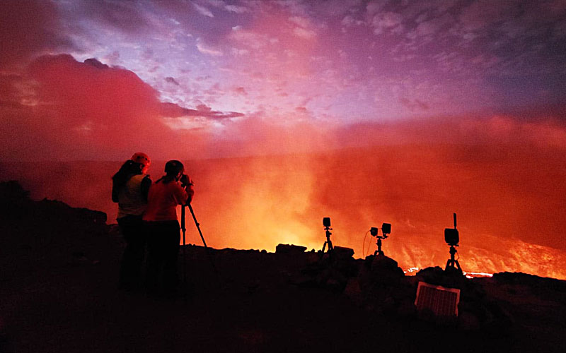 Abigail Nalesnik, master’s student in geology at the University of Delaware, looks through a rangefinder at the eruption in Kīlauea's Halema‘uma‘u crater on the evening of September 30, 2021. She was on the first response team from the U.S. Geological Survey’s Hawaiian Volcano Observatory to visit the eruption and helped monitor and make measurements of the active fountains and lava lake level to track how quickly it was rising. Photo taken from a closed area of Hawaii Volcanoes National Park by Kendra Lynn, USGS.
